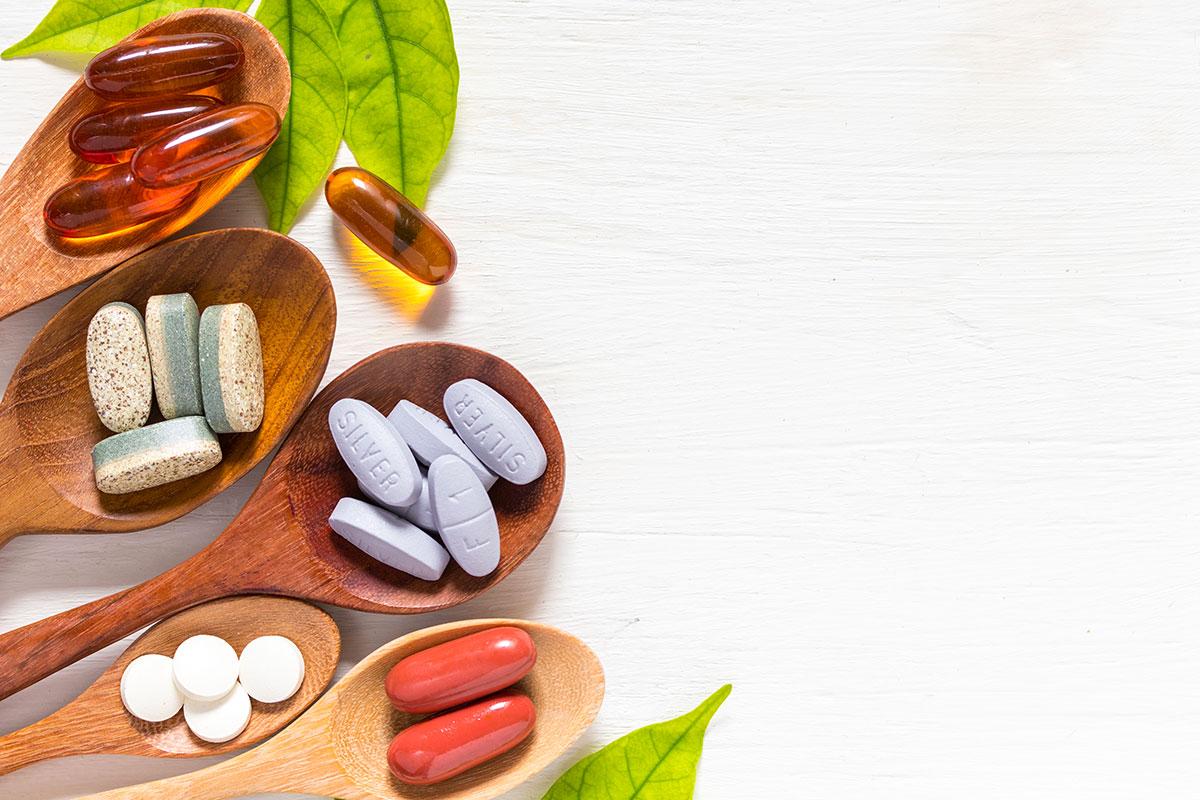 Gélules et comprimés des meilleures vitamines à trouver en pharmacie, présentées dans des cuillères en bois