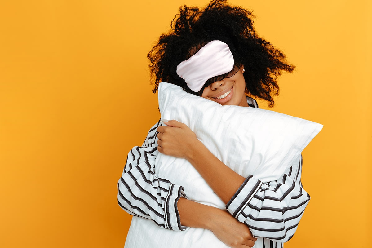 Femme avec un masque de nuit serrant son oreiller sur fond jaune