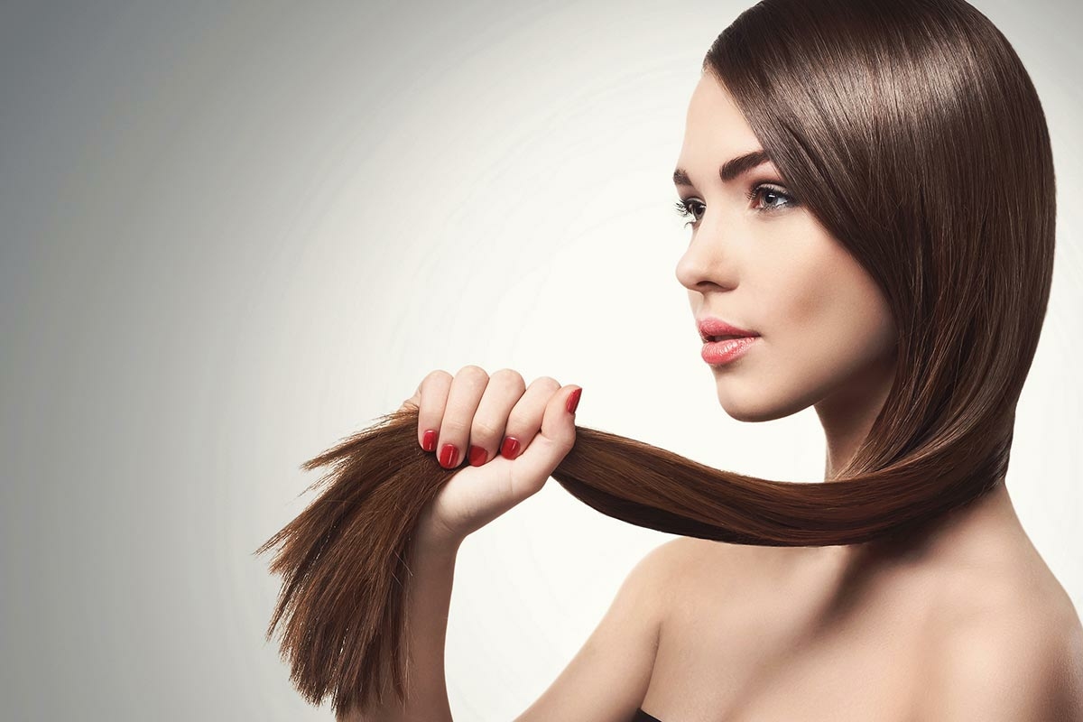 Femme tenant ses longs cheveux, brillants grâce aux vitamines des compléments alimentaires
