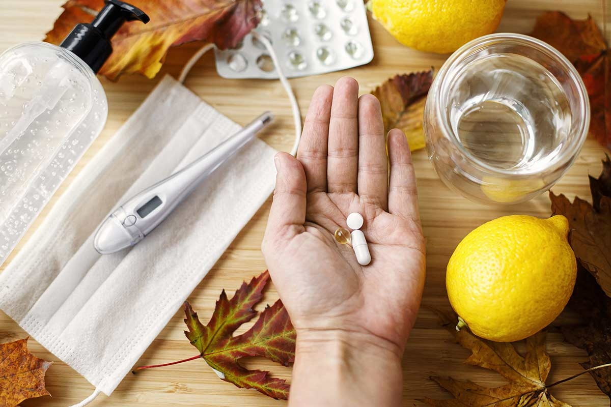 Main contenant des comprimés de vitamine C, un citron, un thermomètre et un masque protecteur